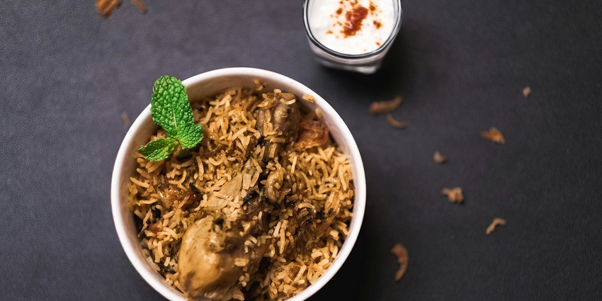 An image of Mughlai cooked white rice and curry with cucumbers served on the side on a plate.