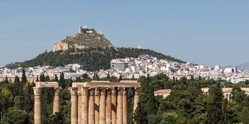 Temple of Olympian Zeus with tall ruined pillars and Athens City in the background.