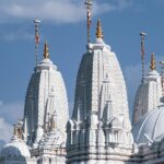 Image of an astonishing white temple in Agra alongside a road with devotees around it.