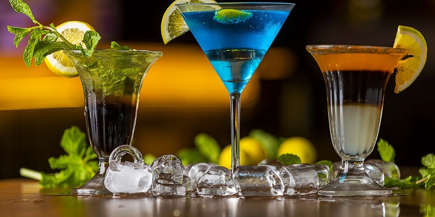 A picture of a bar counter with cocktails placed and ice cubes spilled around