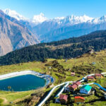 A scenic view of Auli featuring snow covered mountains under a clear blue sky