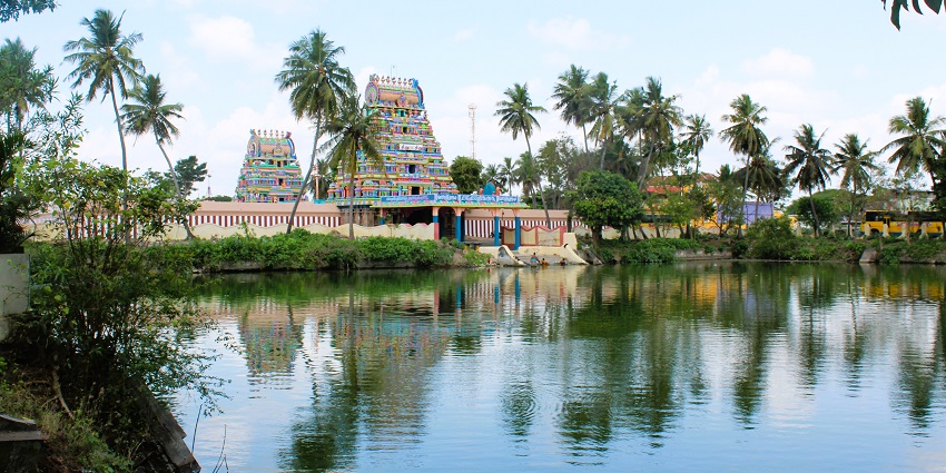 Brahmapureeswarar temple with a lake in front of the entrance, surrounded by greenery.