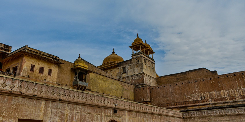 A beautiful tall fort topped with a golden dome standing under a clear blue sky and clouds.