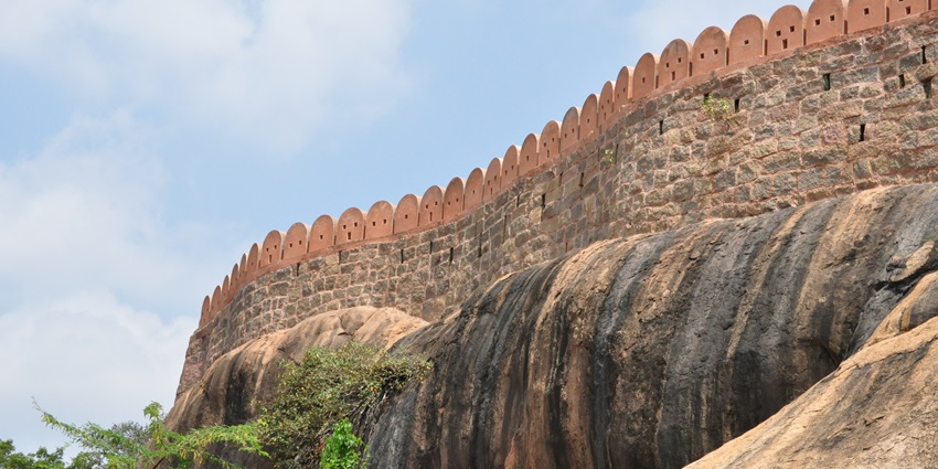 Side view of Thirumayam Fort showing stone walls situated on a rock with small plants beneath