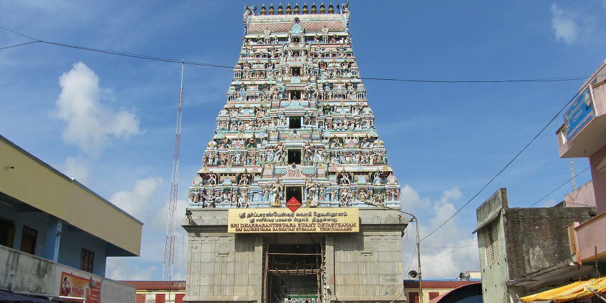 Thirunallar Sani Temple with its entrance tower and statues, surrounded by street shops.