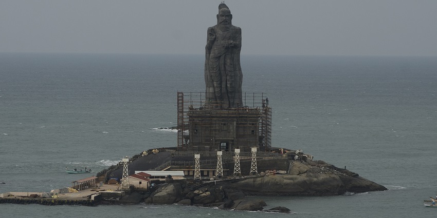 A picture of a tall statue perched upon a rock with the vast ocean in the background