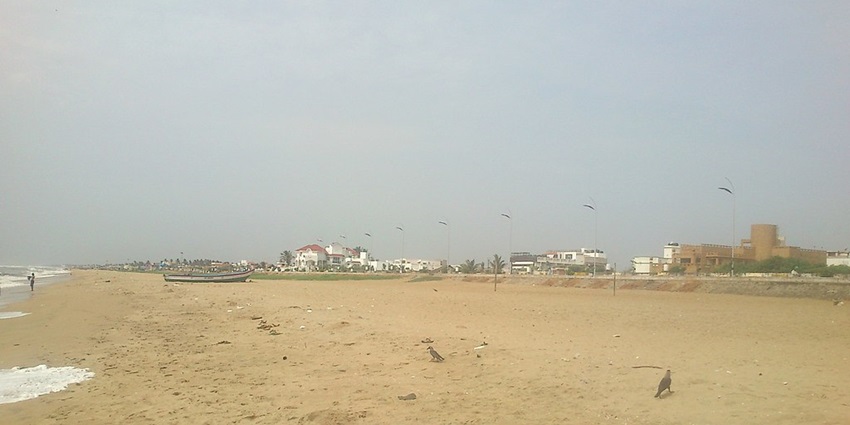 A scenic view of Thiruvanmiyur Beach, featuring golden sands, gentle waves, and a clear blue sky.