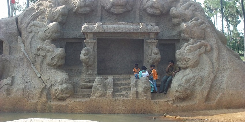 A front of a tiger cave with people sitting and eleven tiger faces carved on the stone.
