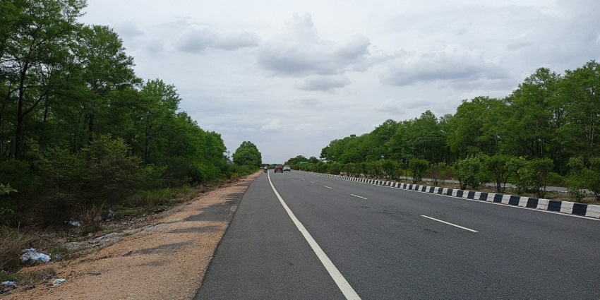 Not a busy highway with multiple lanes, vehicles, and surrounding trees under a cloudy sky.