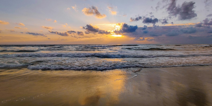 Picturesque view of the beach with waves crashing and vibrant sun setting behind the clouds in Tutcorin