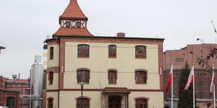 Tyskie Brewing Museum with a clock on top of the building and flags on the sidewalk.