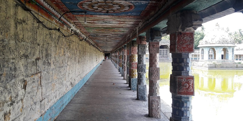 Corridor of a temple with colourful pillars and ceilings and a water reservoir on one side