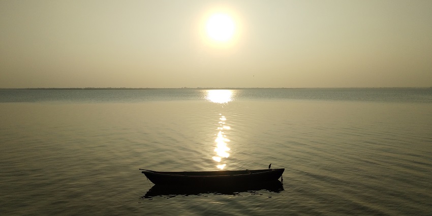 A boat standing in a reservoir of water and the sun casting its shine on the water surface