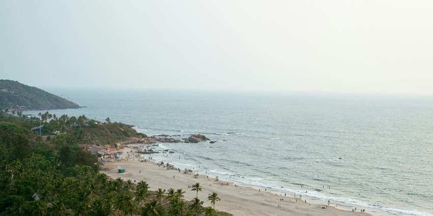 An aerial view of a public beach with tourists enjoying the golden sand and serene waves