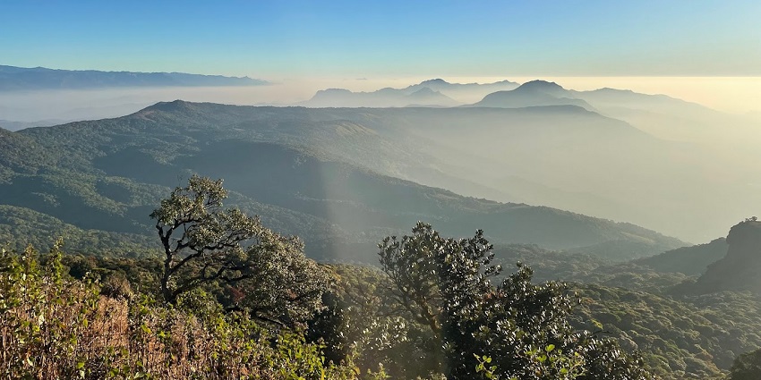 A vast green landscape with wooden railings and distant hills covered in mist and clouds.