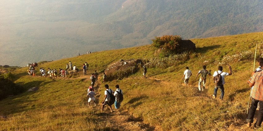 Trekkers navigating the rugged trails of the Velliangiri Mountains, surrounded by greenery.