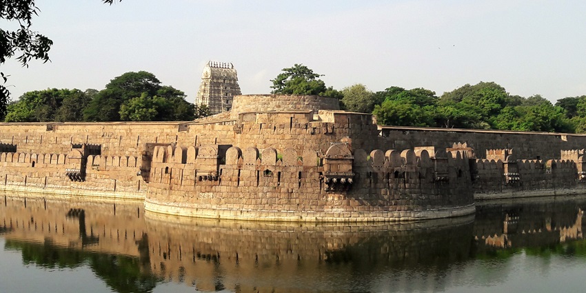 Stoned walls of a Vellore fort with lush greenery in the background and lake in the front.