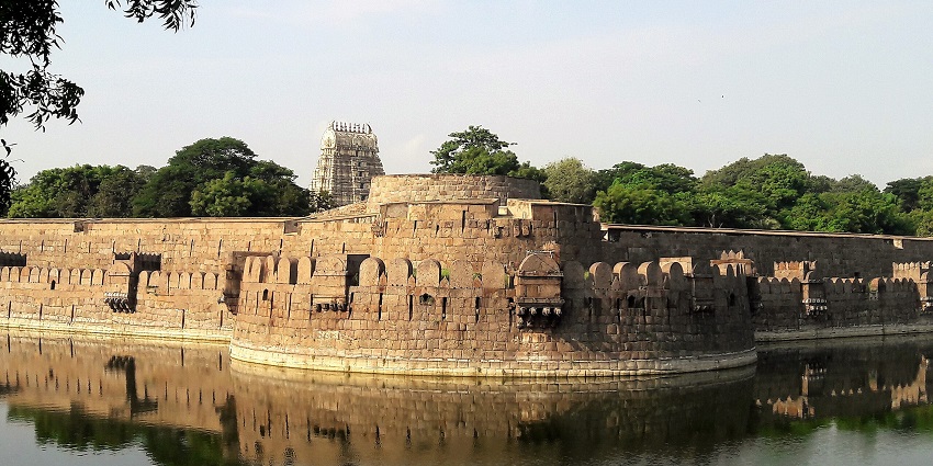 A frontal view of the outer wall of a historical and majestic fort with a pond in front of it