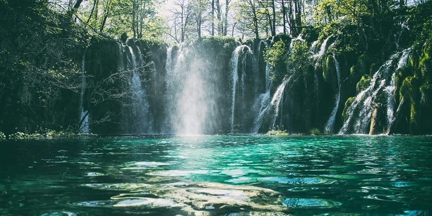 A picturesque view of Vindham Waterfall cascading down rocky cliffs, surrounded by greenery.
