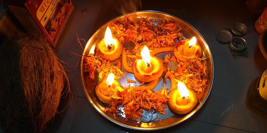 Image of a pooja thali decorated with diya, oil and flowers on a golden colour plate