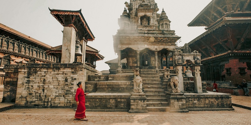 A woman with a red dress walks at the Vindhyavasini Devi temple located in the background.