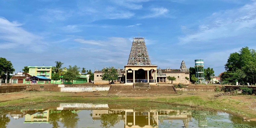 An image of a Hindu temple with a tall tower structure, and a water body circling the wall.