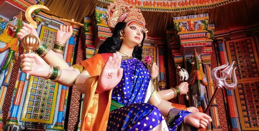 Golden Durga Devi idol adorned with vibrant flowers and jewelry, set against a festive backdrop