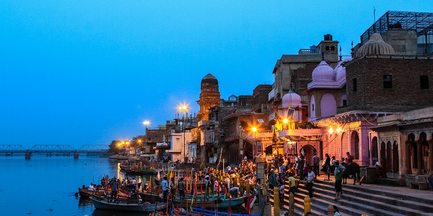 People gathering at Vishram Ghat along the Yamuna River in Mathura, with temples.