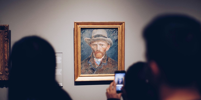 An image of a person taking a pic of an artist wearing a brown hat in the Government Museum.