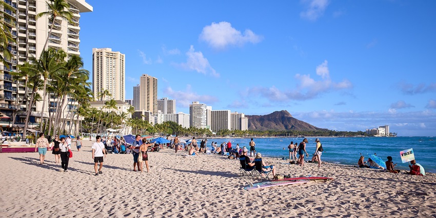 Waikiki Beach with people sitting and enjoying near tall buildings behind palm trees