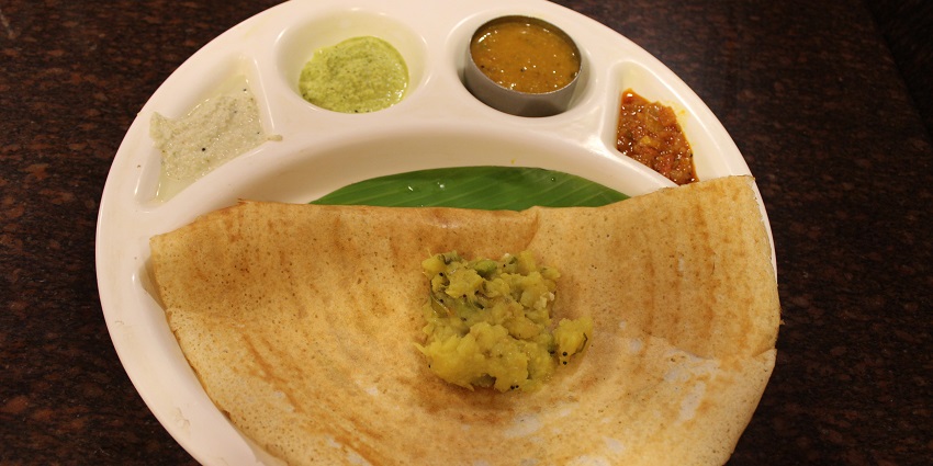 Masala dosa served with sambar and chutneys in traditional Tamil Nadu on a white plate.
