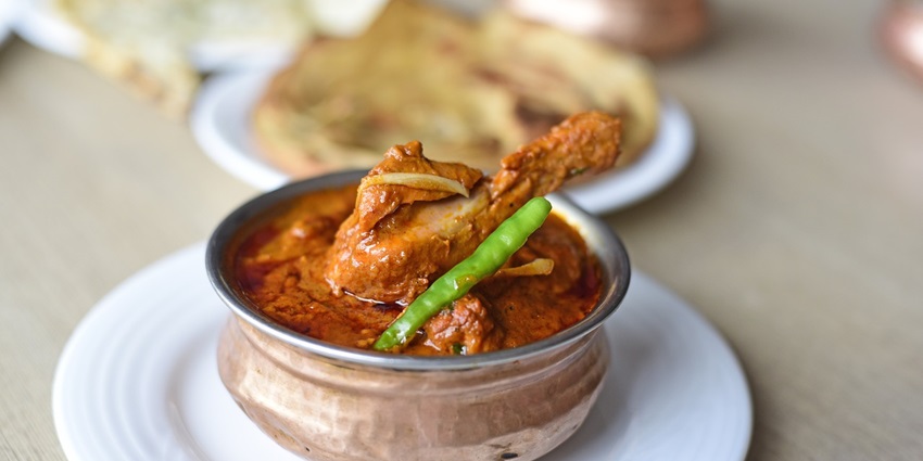 Bowl of spicy curry chicken garnished with herbs, served with rice on a rustic wooden table