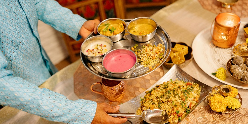 A man in blue shirt serves a plate full of different foods on a table at a restaurant.