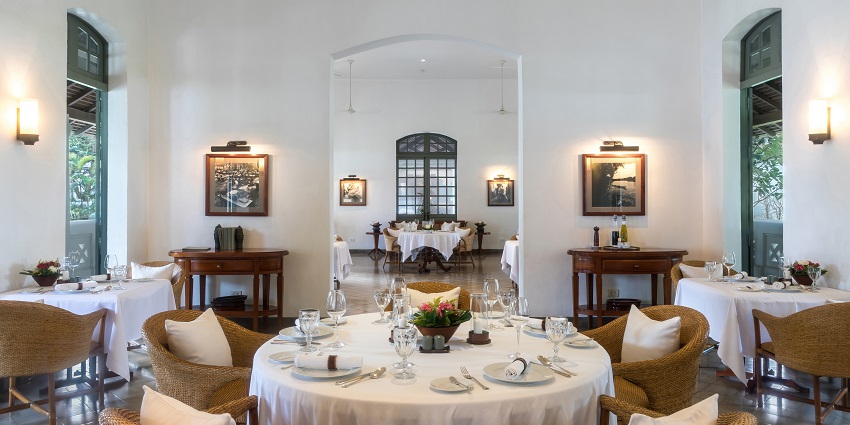 Restaurant shows large glass windows with a large wooden dining table where dining cutlery is set up.
