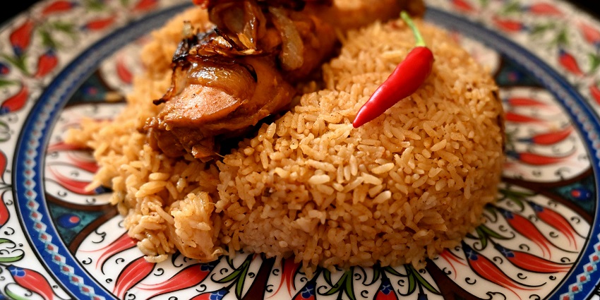 Yellow fried rice on a decorated plate topped with a chicken piece and a red chilli