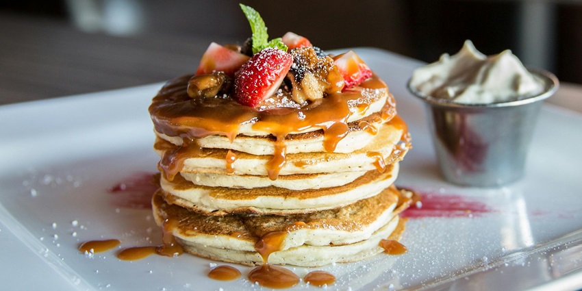 Stack of pancakes garnished with caramel sauce, sliced strawberry, and a mint leaf