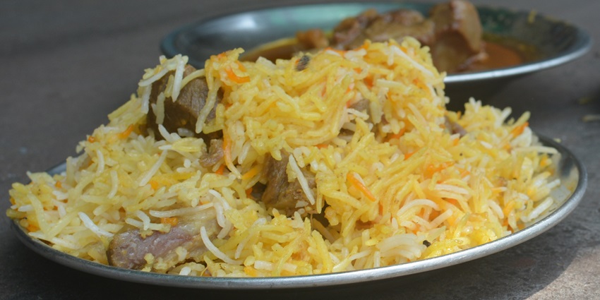 A close-up of a serving of Mutton Biryani on a plate, garnished with fried onions and cilantro.