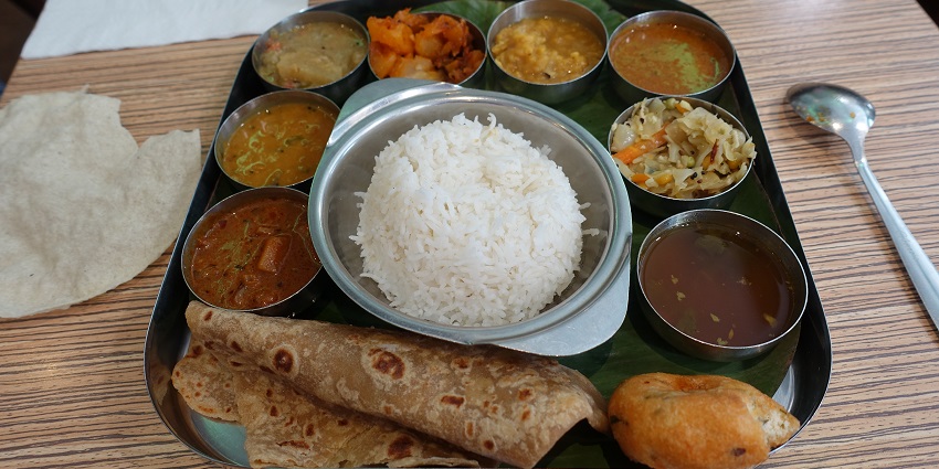 Various South Indian dishes on a banana leaf showcase rice, sambar, veggies, etc.