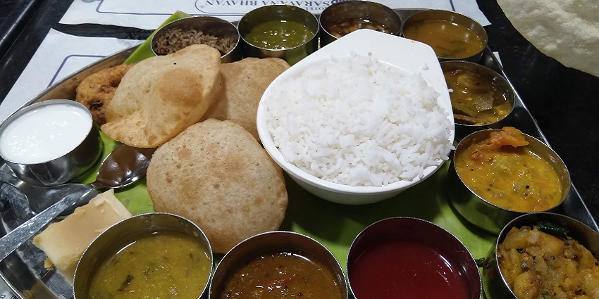 An assortment of South Indian dishes featuring rice, puri etc. served on a banana leaf in a restaurant.