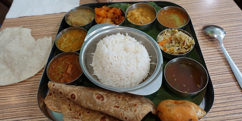 A variety of South Indian dishes served on a banana leaf in a restaurant setting.