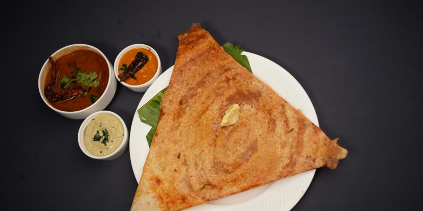 Triangular dosa served on a plate with butter on top and different chutneys and sambar