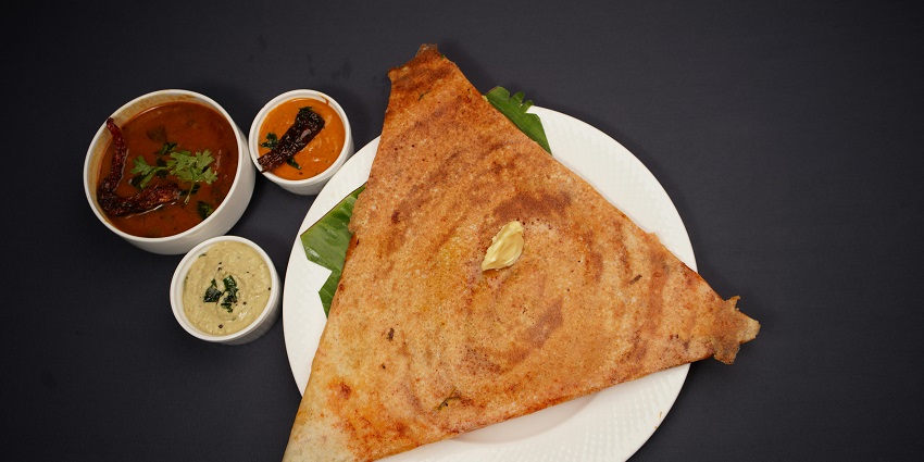 A crispy South Indian dish known as dosa is placed in a plate with other accompaniments