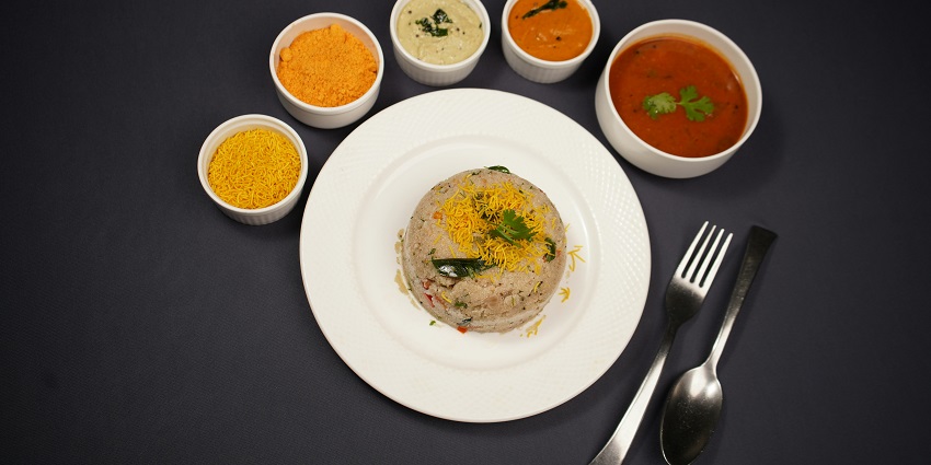 Upma served with sambar, coconut chutney and other items on white bowls and plates.