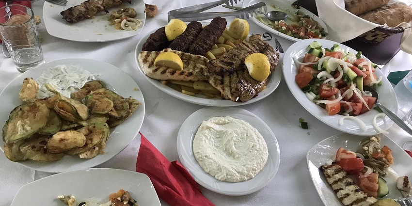 Greek cuisine with multiple dishes, salads, knives and spoons served on white plates.