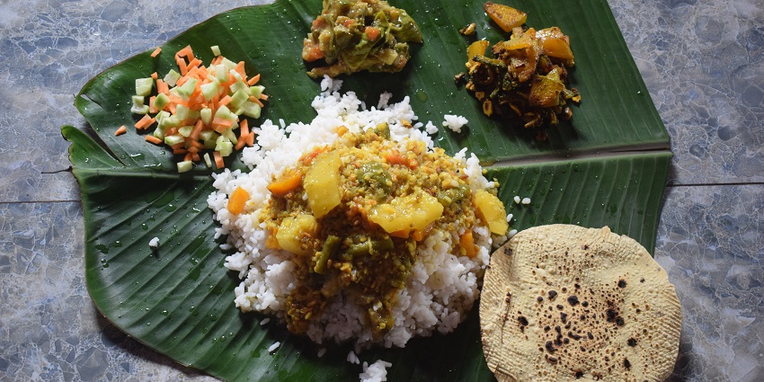 A glimpse of traditional Odia food served on a banana leaf, including rice, curry and veggies.
