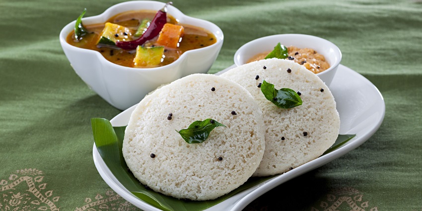 Traditional breakfast of fluffy idlis served on a banana leaf with chutney and sambar