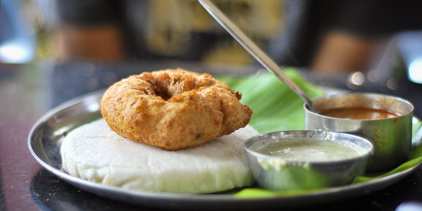 Idli and vada served on a banana leaf over a silver plate with chutney and sambar
