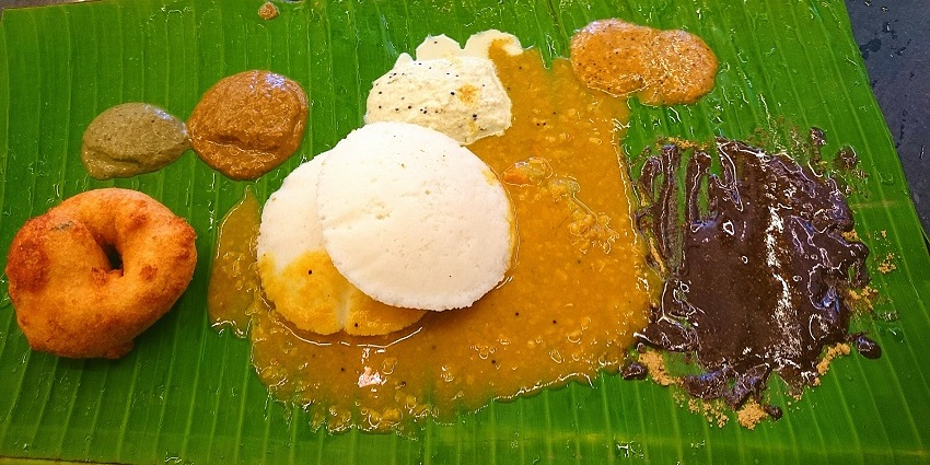 Traditional South Indian meal with sambar, vada, and idli served on a banana leaf.