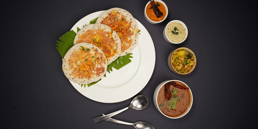 Big-sized Idlis served on a banana leaf and plate with sambar and different chutneys.