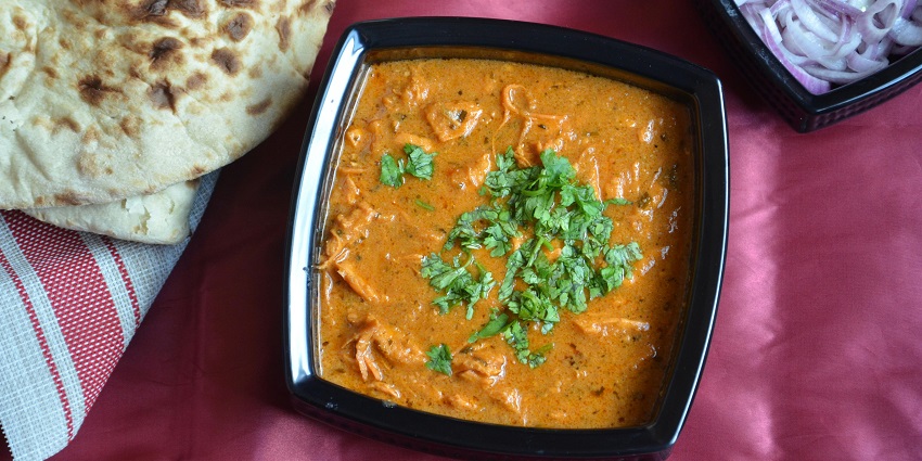 Curry served in a bowl topped with coriander sliced onions and bread placed alongside.